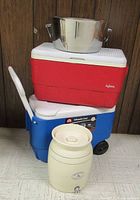 Stacked view of stainless tub, red Igloo cooler, blue Igloo Wheelie Cool cooler, Neiman Marcus crock