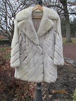 Front view of off-white fur coat on hanger showing diagonal panel design and large fur collar