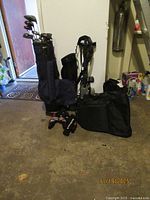 Full view of golf clubs in bag, push cart, travel bag on floor