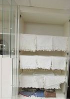 Cabinet shelves with multiple folded white lace linens and colored fabrics