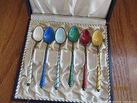 Open case showing six enamel spoons arranged in satin interior