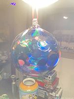 Large iridescent blown glass ball ornament hanging by red ribbon