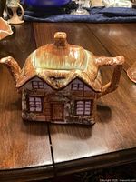 Front view of ceramic cottage-shaped teapot showing lid, door, windows and spout
