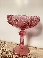 Side view of dusty rose Fenton footed comport showing raised cabbage rose pattern and scalloped rim