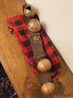 Full view of leather strap showing five brass bells on red-black plaid cloth