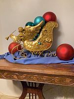 Gold metal sleigh with four ornament balls on wood table