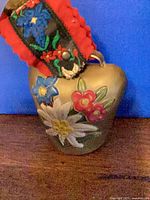 Front of gold cow bell showing painted alpine flowers and part of strap
