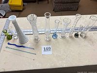 Front view of all ten bud vases and three swizzle sticks on table with rulers for scale
