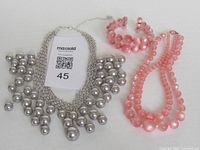 Overview of all three jewelry pieces: silver bib necklace, pink necklace, pink bracelet