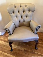 Front view of tufted beige armchair showing upholstery, tufting, nailhead trim and cabriole legs