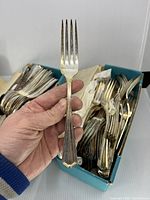 Hand holding one fork in front of box containing remaining forks