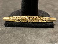 Front view of filigree gold tie bar on stand