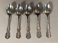 Five matching sterling silver spoons side by side