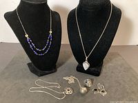 All six jewelry items displayed: two necklaces on busts, four items on surface