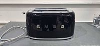 Front view of SMEG black gloss toaster showing logo and exterior condition