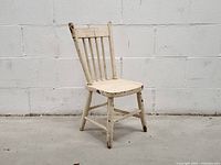 Front left view of antique white wooden doll chair showing seat, slat back, worn paint