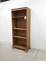 Full front view of tall oak finish bookcase with four shelf openings on casters