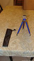 Blue aluminum tripod opened on table with black pouch beside it