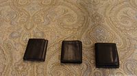 Three closed dark leather bifold wallets on patterned surface