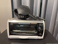 Front view of Black & Decker toaster oven with two black utensils stacked on top