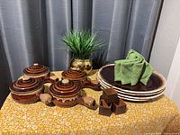 Four ceramic soup bowls with lids, stack of plates, napkins and napkin rings on table