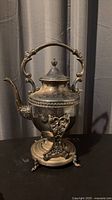 Full view of silver on copper teapot on stand with burner