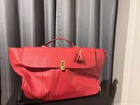 Front view of Joy Mangano red roller bag with fold-over flap and clasp