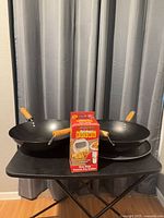 Two woks, sealed fry cutter box, pizza pan displayed on table