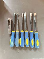 Five wood carving chisels with blue/yellow handles and one steel circle punch on dark surface