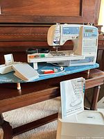 Overall view of sewing machine on ironing board with accessories and manual visible
