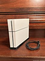 Front angled view of white PS4 on stand with power cable beside