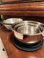 Nested stainless bowls showing black bases and colander behind