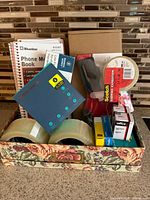 Overview of boxed lot showing phone books, tape rolls, Scotch dispenser, staples, floral box