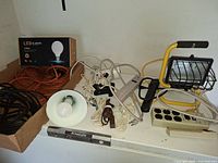 All items on shelf showing cords, power bars, light fixtures, bulb box