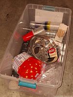 Large plastic tote holding assorted cups, cutlery, napkins, straws, lids, stainless bowl