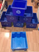 stacked view of six blue recycle bins with logos and one lighter blue bin without logo