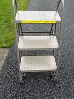 Front view of three-step metal rolling ladder on casters