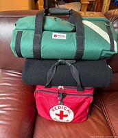 Stacked view of green oxygen bag, black blanket and red first aid bag