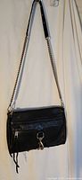 Front view of black leather Rebecca Minkoff crossbody bag hanging, showing chain strap and front clasp