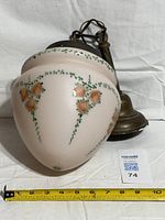 Side view of glass shade with roses and attached metal canopy, measuring tape visible