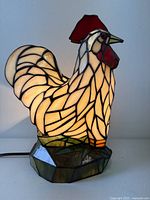 Front left view of stained glass rooster lamp illuminated