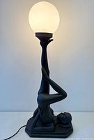 Entire lamp illuminated showing nude figure base and frosted globe shade