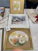 Three framed artworks laid on countertop: daffodils watercolour, winter cottage print, poppies watercolour