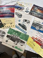 Spread of assorted auto brochures showing Frontenac, Riley, Volkswagen, Meteor and others
