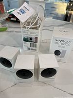 Three Wyze Cam Outdoor cameras, open box with cables, additional sealed box
