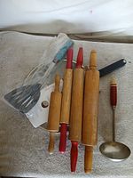 Group shot of rolling pins, ladle, spatula in plastic, black-handled utensil and round tray