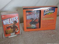 Both sealed Wheaties boxes side by side: Muhammad Ali in acrylic case, Tiger Woods in commemorative sleeve
