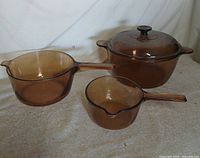 Three amber glass saucepans displayed together on fabric background