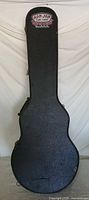 Full front view of closed black hard guitar case with Ron Jon badge