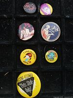 Overall view of seven visible pinbacks arranged in tray